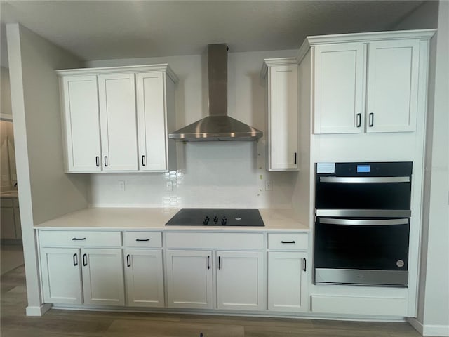 kitchen with black appliances, white cabinets, wall chimney range hood, hardwood / wood-style floors, and backsplash