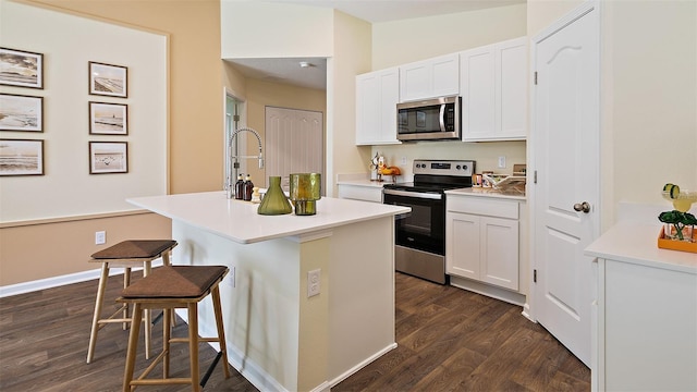 kitchen with a kitchen island with sink, dark hardwood / wood-style floors, a breakfast bar area, white cabinets, and appliances with stainless steel finishes