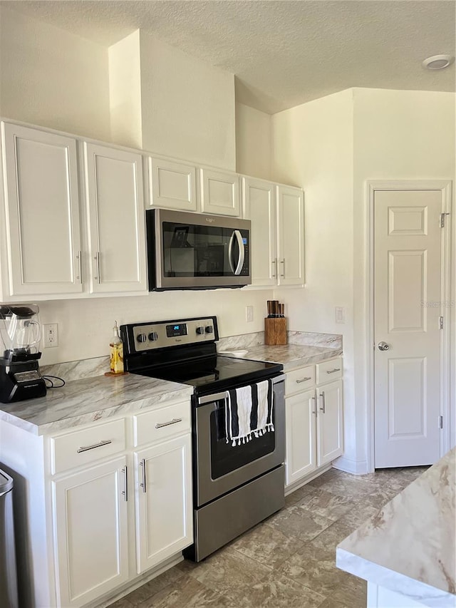 kitchen featuring white cabinetry, stainless steel appliances, light stone counters, and a textured ceiling