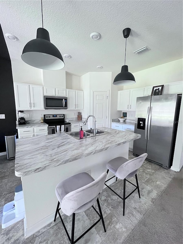 kitchen with an island with sink, sink, white cabinets, pendant lighting, and appliances with stainless steel finishes