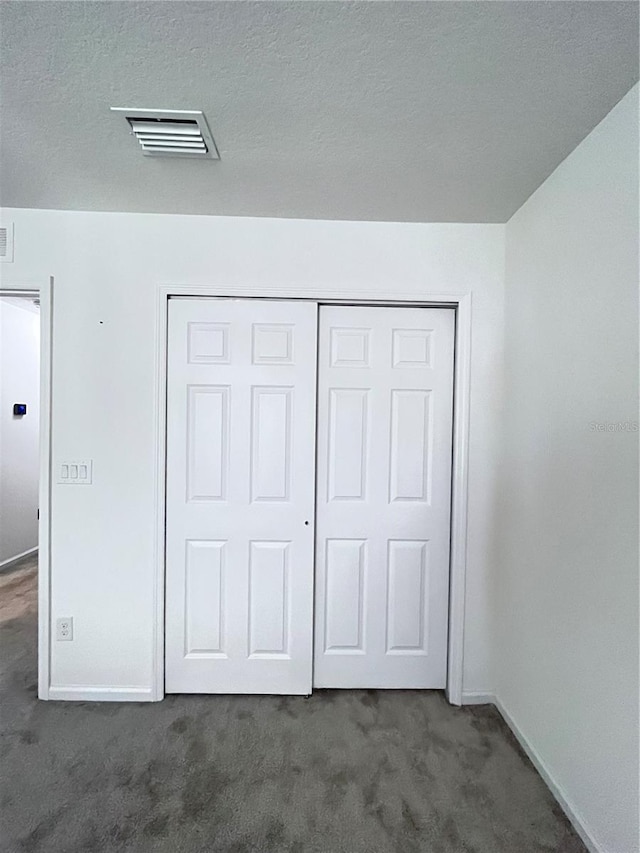 unfurnished bedroom featuring dark carpet, a textured ceiling, and a closet