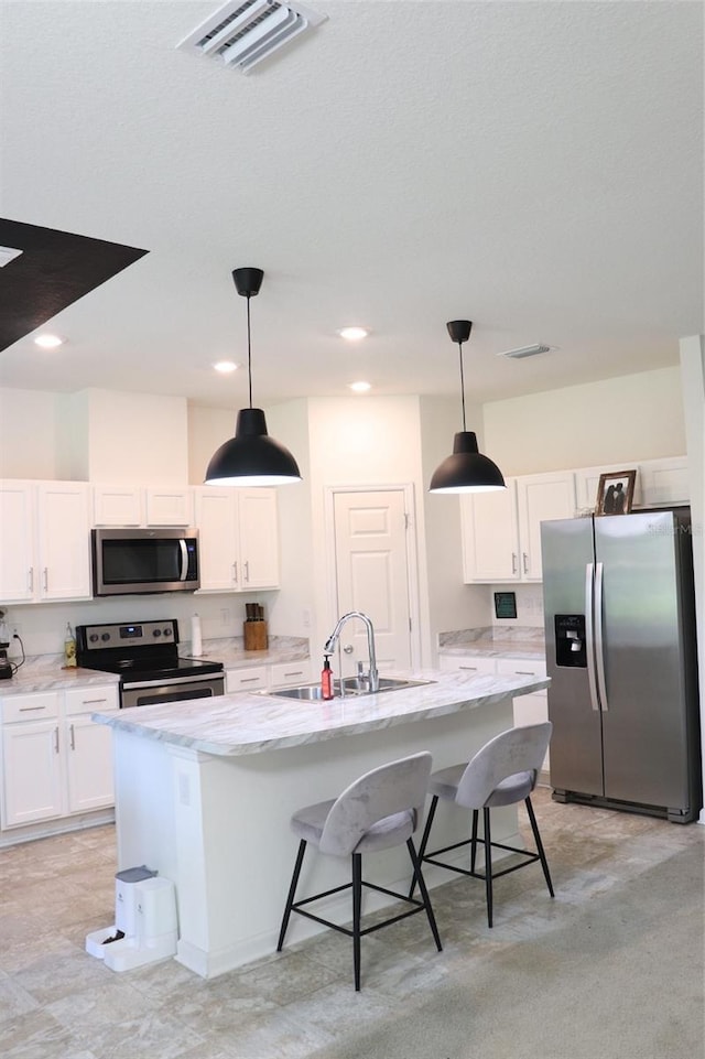 kitchen with sink, white cabinetry, stainless steel appliances, decorative light fixtures, and a center island with sink