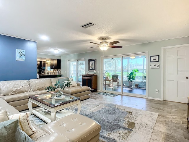 living room with ceiling fan, crown molding, a textured ceiling, and sink