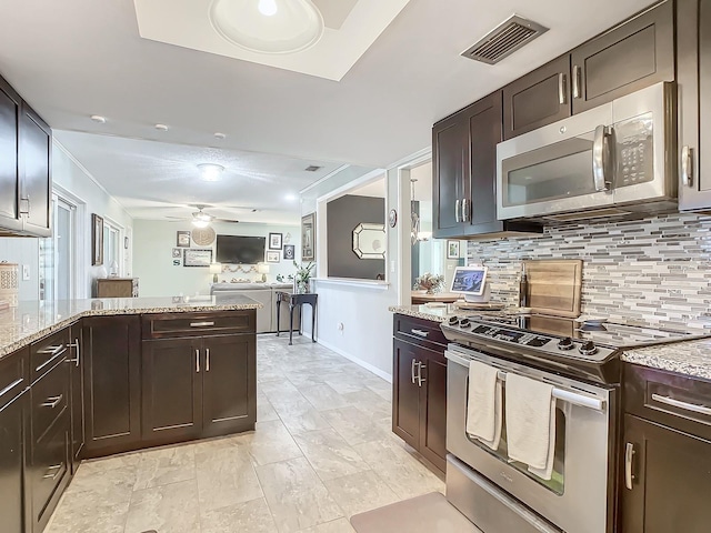 kitchen featuring light stone countertops, dark brown cabinets, ceiling fan, stainless steel appliances, and decorative backsplash