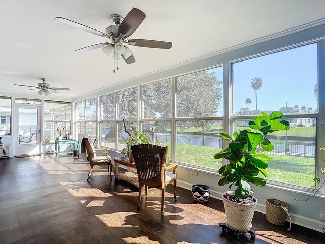 sunroom / solarium featuring baseboards, wood finished floors, a water view, and crown molding