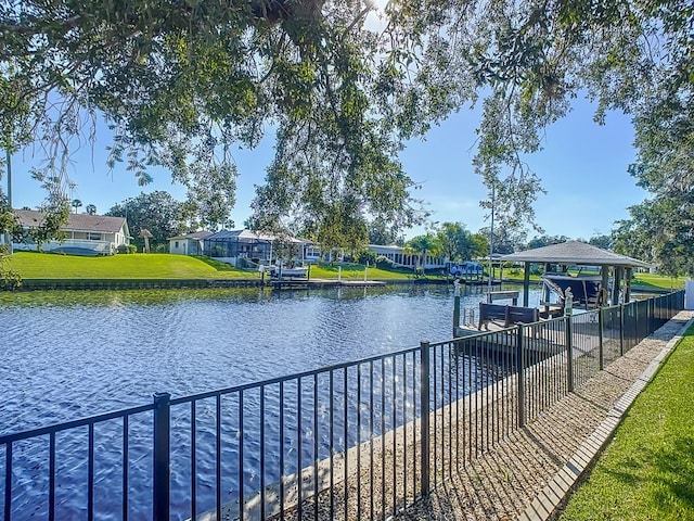 view of dock featuring boat lift, fence, a yard, and a water view