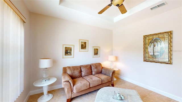 living room featuring ceiling fan, light tile patterned floors, and a raised ceiling