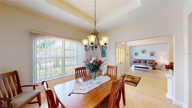 dining space with an inviting chandelier, a tray ceiling, a healthy amount of sunlight, and light tile patterned floors