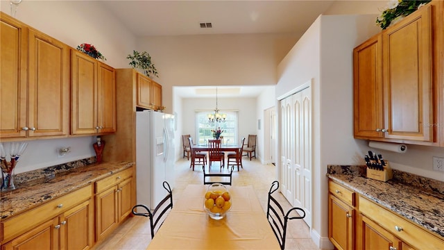 kitchen with white fridge with ice dispenser, pendant lighting, light stone counters, light tile patterned floors, and a chandelier