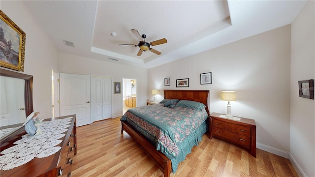 bedroom featuring light hardwood / wood-style flooring, a closet, a raised ceiling, and ceiling fan