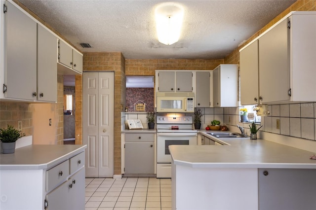 kitchen featuring white appliances, light tile patterned flooring, sink, a textured ceiling, and kitchen peninsula