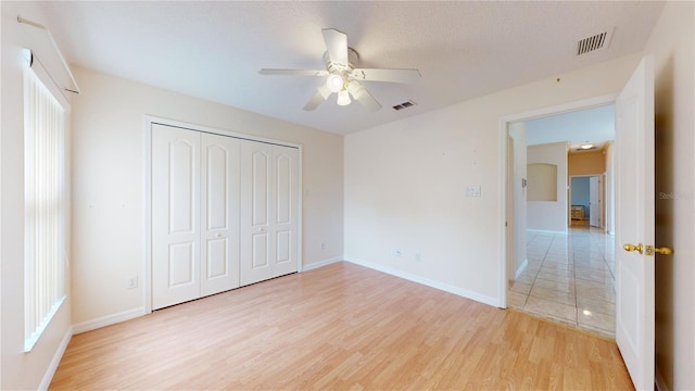 unfurnished bedroom with light hardwood / wood-style floors, a textured ceiling, a closet, and ceiling fan