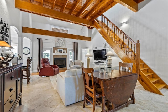 living room featuring a towering ceiling, light tile patterned flooring, a tiled fireplace, wooden ceiling, and beam ceiling