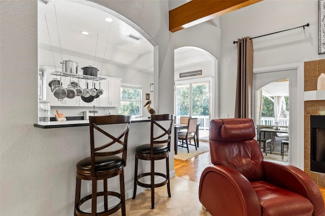 bar featuring a tile fireplace, white cabinetry, light hardwood / wood-style floors, and plenty of natural light