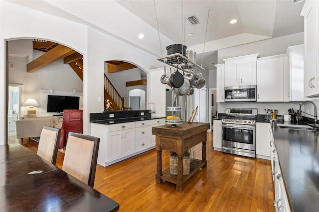 kitchen featuring hardwood / wood-style flooring, appliances with stainless steel finishes, sink, and vaulted ceiling with beams