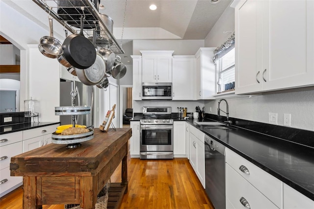 kitchen with appliances with stainless steel finishes, white cabinets, hardwood / wood-style flooring, and sink