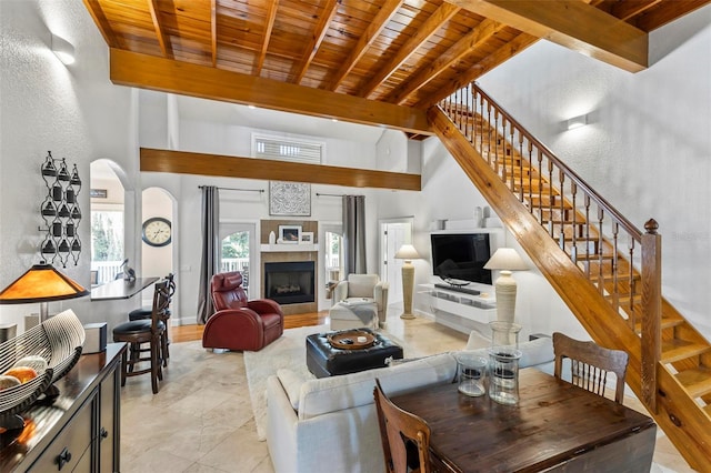 living room with a tiled fireplace, beamed ceiling, wooden ceiling, and a high ceiling