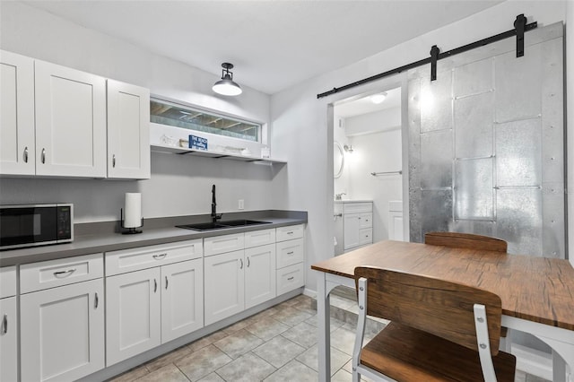 kitchen with sink, a barn door, white cabinetry, and light tile patterned floors