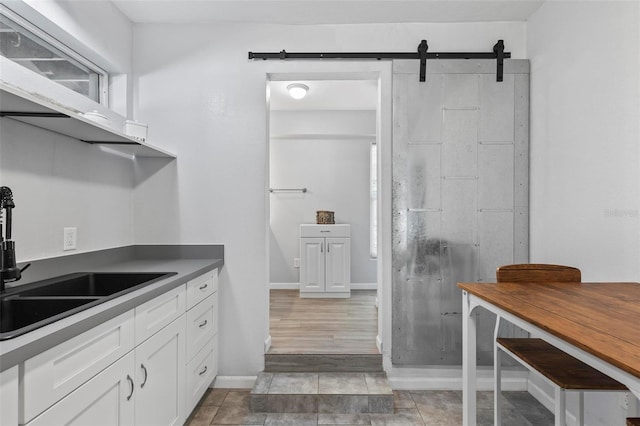 kitchen with white cabinetry, a barn door, sink, and light wood-type flooring