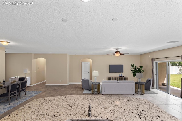 tiled living area featuring visible vents, a textured ceiling, arched walkways, and a ceiling fan