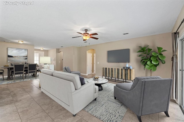 living area featuring arched walkways, a textured ceiling, light tile patterned flooring, visible vents, and a ceiling fan