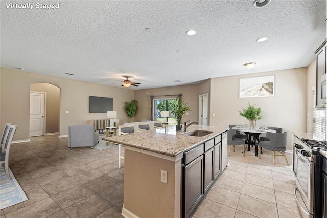 kitchen featuring arched walkways, a breakfast bar area, appliances with stainless steel finishes, a kitchen island with sink, and a sink