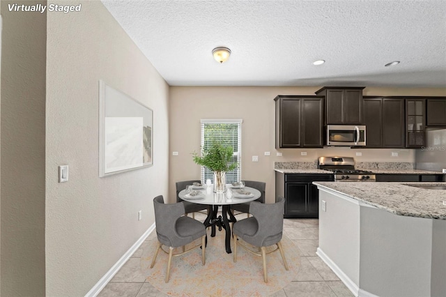 kitchen featuring light tile patterned flooring, appliances with stainless steel finishes, light stone counters, dark brown cabinetry, and a textured ceiling