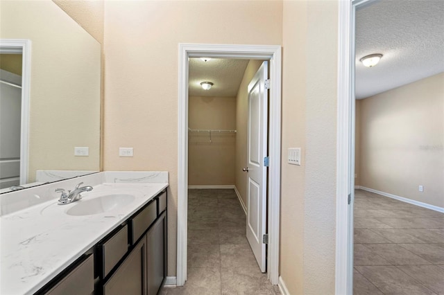 bathroom featuring a spacious closet, a textured ceiling, vanity, tile patterned flooring, and baseboards