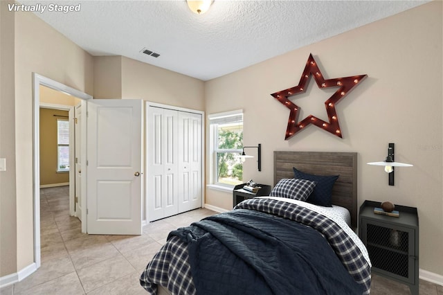 bedroom with a textured ceiling, light tile patterned floors, visible vents, baseboards, and a closet