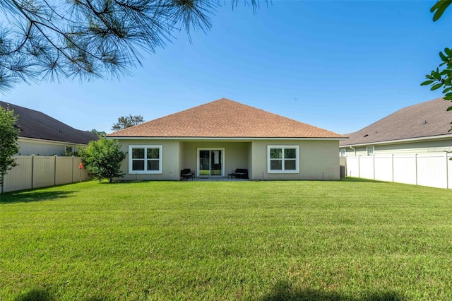 back of house featuring a shingled roof, a fenced backyard, a yard, and stucco siding