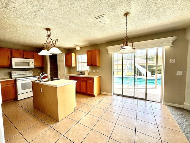 kitchen with white appliances, sink, decorative light fixtures, and a center island with sink