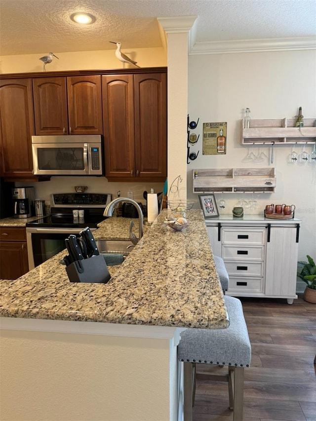 kitchen with stainless steel appliances, light stone countertops, dark hardwood / wood-style floors, and kitchen peninsula