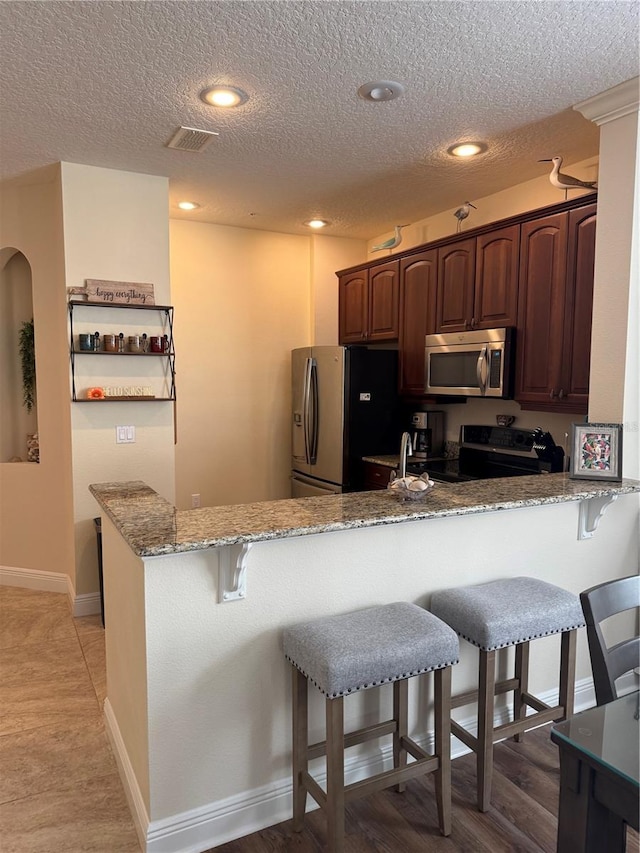 kitchen featuring appliances with stainless steel finishes, a breakfast bar area, light hardwood / wood-style floors, kitchen peninsula, and light stone countertops