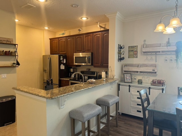 kitchen with appliances with stainless steel finishes, hardwood / wood-style floors, a breakfast bar area, kitchen peninsula, and light stone countertops