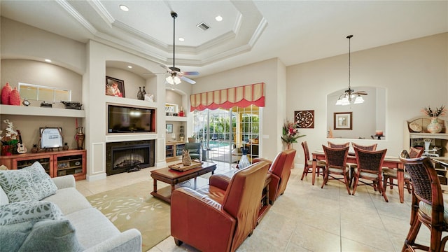 tiled living room featuring ceiling fan, crown molding, built in features, and a raised ceiling