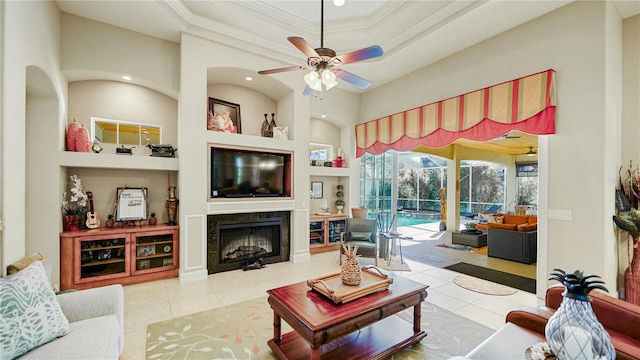 tiled living room with a tiled fireplace, ceiling fan, crown molding, and built in shelves