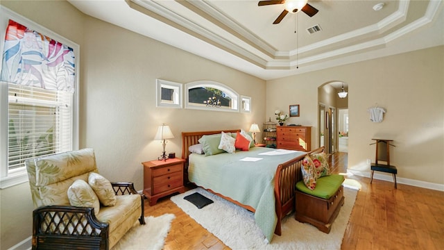 bedroom featuring crown molding, a tray ceiling, light wood-type flooring, and ceiling fan