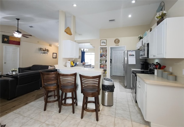 kitchen with lofted ceiling, a breakfast bar area, kitchen peninsula, stainless steel appliances, and white cabinets