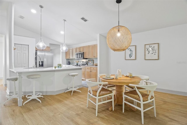 dining room with sink, light wood-type flooring, and vaulted ceiling