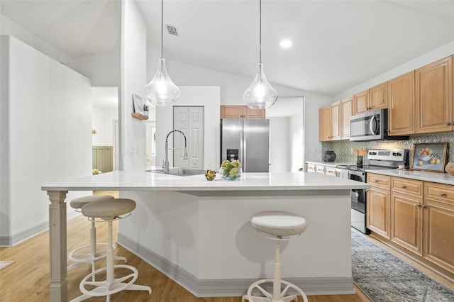 kitchen with a kitchen island with sink, a breakfast bar area, sink, vaulted ceiling, and appliances with stainless steel finishes