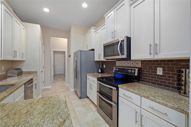 kitchen with light stone countertops, appliances with stainless steel finishes, decorative backsplash, white cabinetry, and light tile patterned flooring