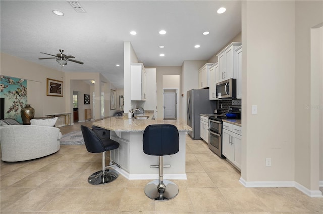 kitchen with light stone countertops, stainless steel appliances, a kitchen breakfast bar, kitchen peninsula, and white cabinets