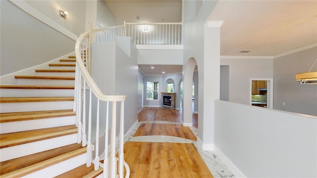 foyer with a towering ceiling, crown molding, wood-type flooring, and a fireplace