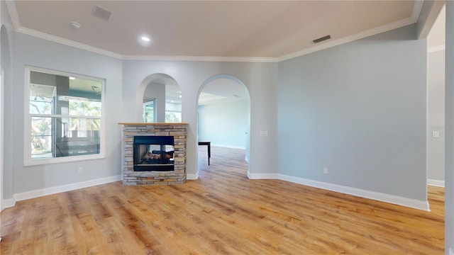 unfurnished living room with crown molding, a stone fireplace, and light wood-type flooring