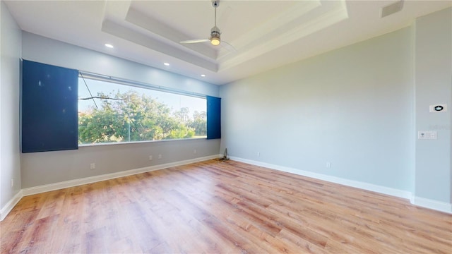 empty room with light hardwood / wood-style flooring, a tray ceiling, and ceiling fan