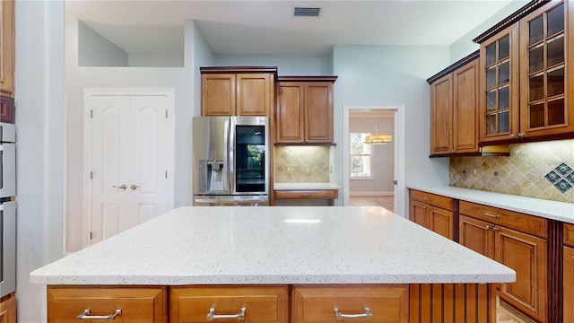 kitchen featuring light stone counters, a kitchen island, backsplash, and stainless steel fridge with ice dispenser