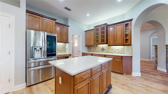 kitchen with tasteful backsplash, a center island, light hardwood / wood-style floors, light stone counters, and stainless steel refrigerator with ice dispenser