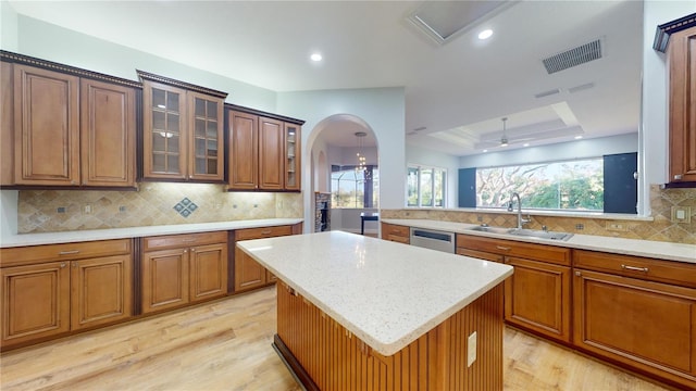 kitchen featuring a raised ceiling, backsplash, a kitchen island, light wood-type flooring, and sink