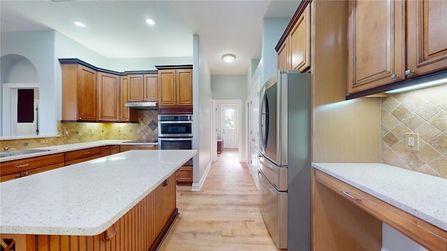 kitchen featuring appliances with stainless steel finishes, a kitchen island, backsplash, light stone counters, and light hardwood / wood-style flooring