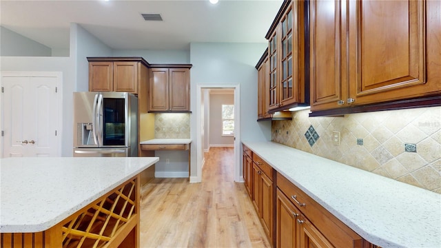 kitchen with light hardwood / wood-style floors, stainless steel fridge with ice dispenser, light stone counters, and backsplash